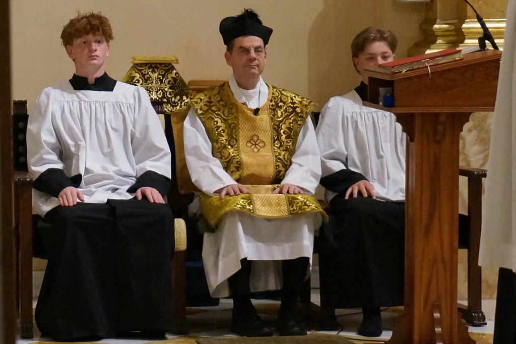 The Rev. John Ubel, pastor of the Church of Saint Agnes, wears the traditional biretta hat and vestments as he sits between altar servers during one of the Catholic parish’s Latin Masses in St. Paul, Minn., Sunday, June 28, 2026. (AP Photo/Giovanna Dell’Orto)