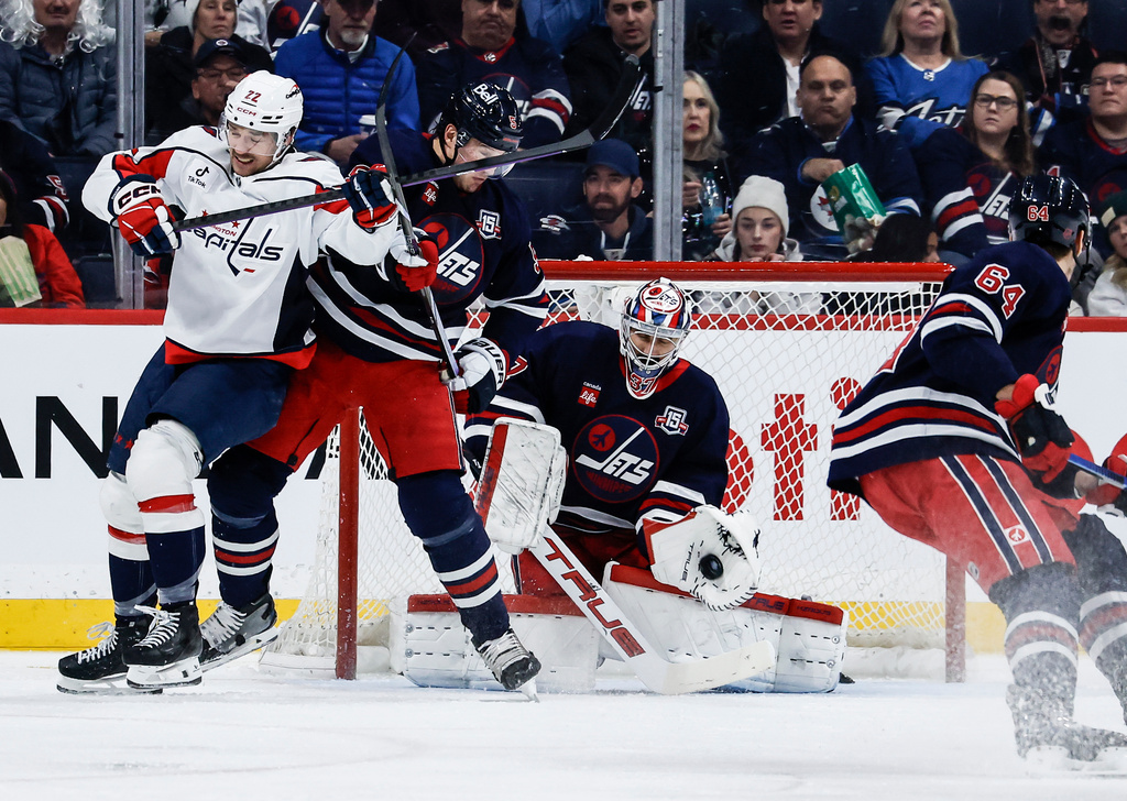 Winnipeg Jets goaltender Connor Hellebuyck (37) saves the shot as Luke Schenn (5) defends against Washington Capitals' Brandon Duhaime (left) during the second period of an NHL game in Winnipeg on Saturday, Dec. 13, 2025. (John Woods/The Canadian Press via AP)