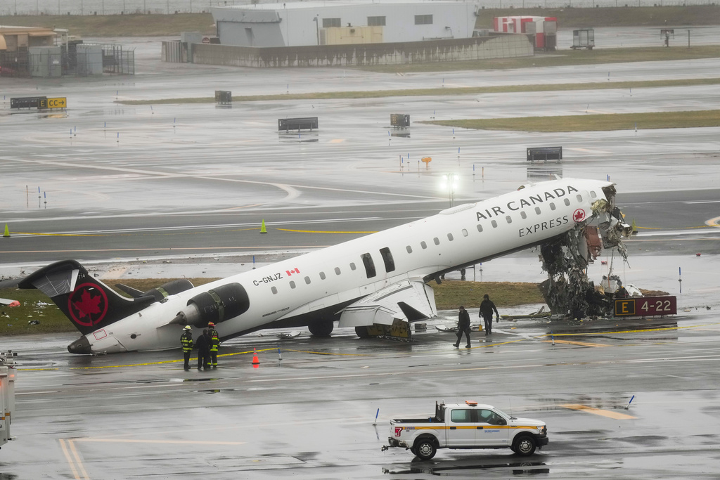 Firefighters and investigators examine the site, Monday, March 23, 2026, where an Air Canada jet came to rest after colliding with a Port Authority firetruck at LaGuardia Airport, after landing Sunday night in New York. (AP Photo/Seth Wenig)