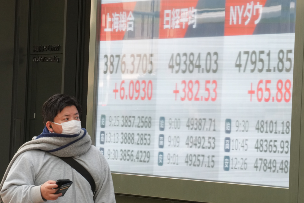 A person walks in front of an electronic stock board showing the market indexes of Shanghai, Tokyo and New York Dow at a securities firm Friday, Dec. 19, 2025, in Tokyo. (AP Photo/Eugene Hoshiko)