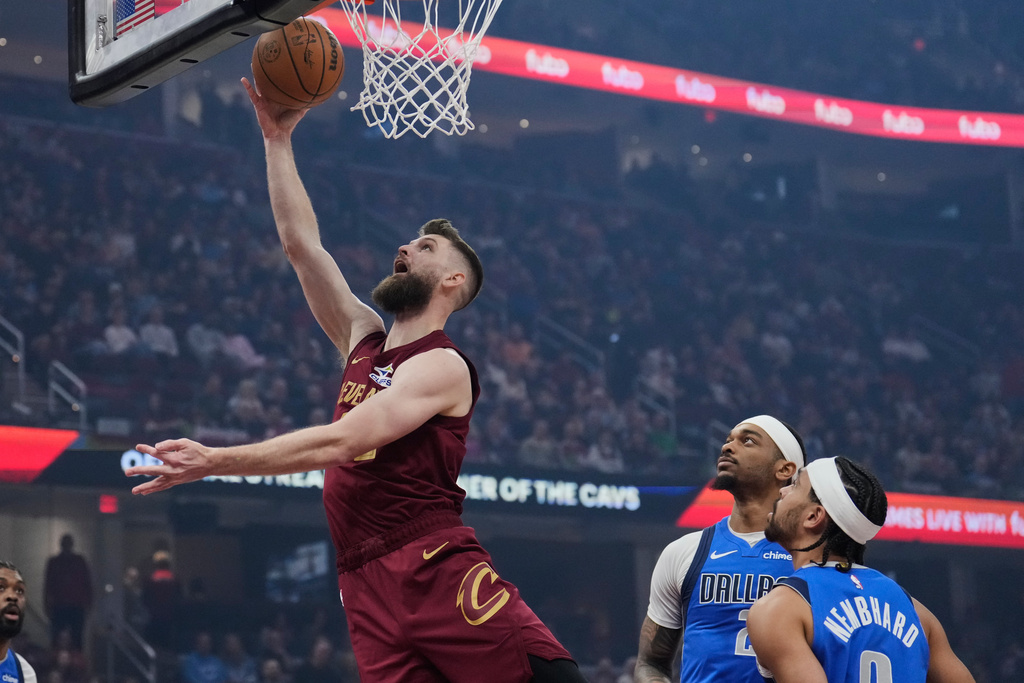Cleveland Cavaliers forward Dean Wade, left, shoots in front of Dallas Mavericks forward P.J. Washington, center, and guard Ryan Nembhard, right, in the first half of an NBA basketball game in Cleveland, Sunday, March 15, 2026. (AP Photo/Sue Ogrocki)