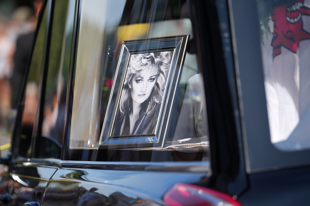 A hearse with the coffin and a picture of singer Bonnie Tyler moves through the streets past fans ahead of her funeral in Mumbles, Wales, Saturday, Aug. 15, 2026. (AP Photo/Alastair Grant)