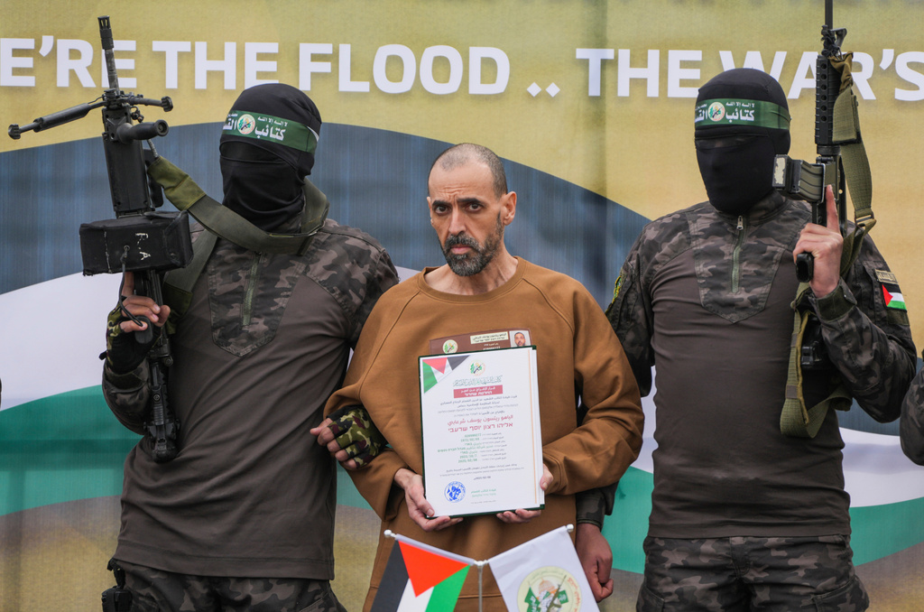 Israeli captive Eli Sharabi who has been held hostage by Hamas in Gaza since Oct. 7, 2023, stands on a stage escorted by Hamas fighters before being handed over to the Red Cross in Deir al-Balah, central Gaza Strip, Saturday Feb. 8, 2025. (AP Photo/Abdel Kareem Hana)