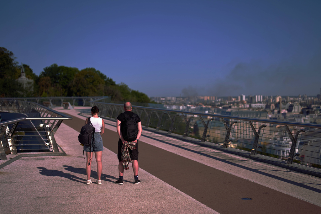 People observe a daily nationwide minute of silence in memory of soldiers killed in the war with Russia as smoke rises from the city following a Russian missile attack in Kyiv, Sunday, Aug. 16, 2026. (AP Photo/Francisco Seco)