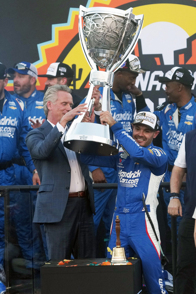 Kyle Larson receives the trophy from NASCAR Commissioner Steve Phelps after winning the NASCAR Cup Series championship Sunday, Nov. 2, 2025, in Avondale, Ariz. (AP Photo/Rick Scuteri)