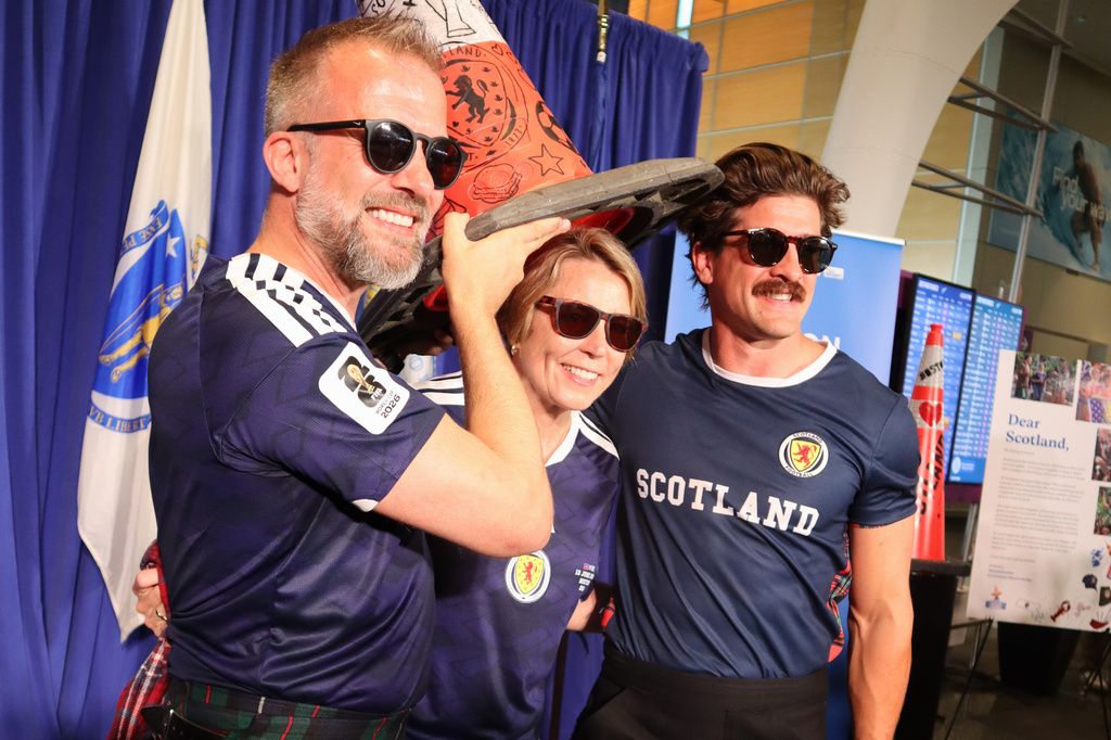 Massachusetts Gov. Maura Healey, center, poses with Scottish football fans Andrew Dobbie, left, and Danny Campbell while wearing the commemorative Boston Cone during a welcoming ceremony at Boston Logan International Airport, Tuesday, July 14, 2026, in Boston. (AP Photo/Leah Willingham)