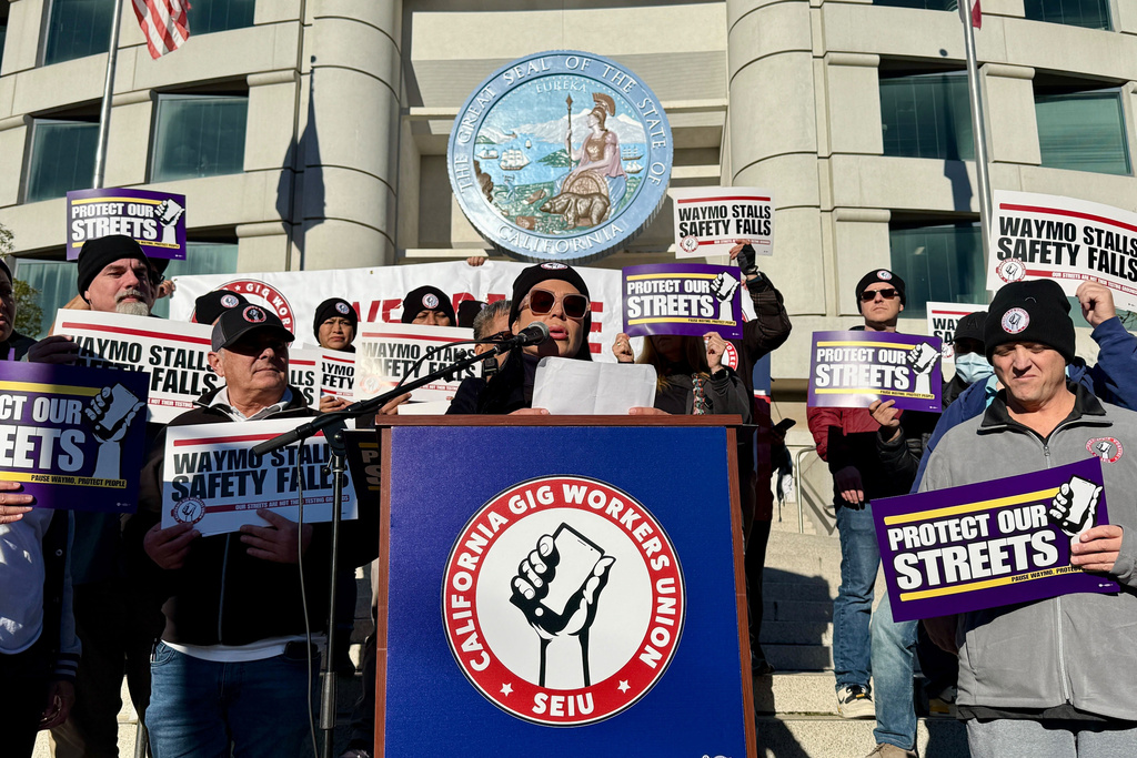 Demonstrators holds signs during a protest by Uber and Lyft drivers asking state regulators to take self-driving taxis off the streets due to safety concerns at the California Public Utilities Commission headquarters Friday, Jan. 9, 2026, in San Francisco. (AP Photo/Haven Daley)