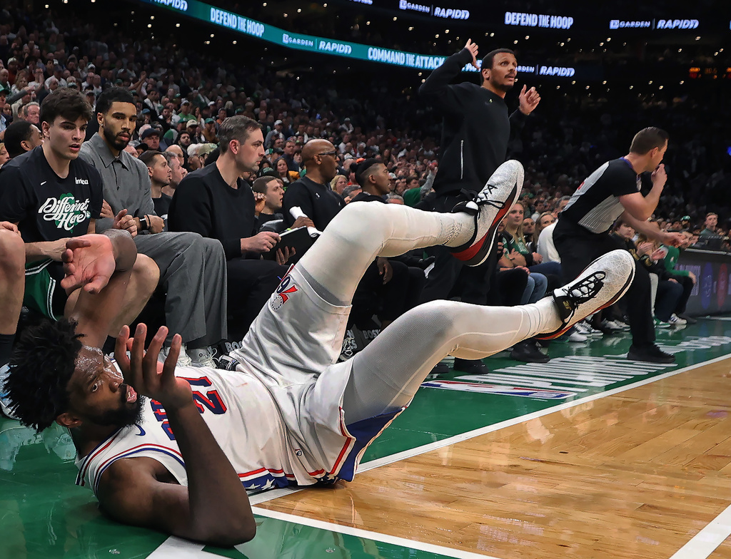 Philadelphia 76ers' Joel Embiid dives onto the ground in pursuit of a loose ball in front of the Boston Celtics bench late in the fourth quarter. Celtics head Joe Mazzulla is standing in the center, while injured Celtics player Jayson Tatum (in grey at left) looks on during Game 7 of a first round NBA basketball playoffs series, Saturday, May 2, 2026 in Boston. (AP Photo/Jim Davis)