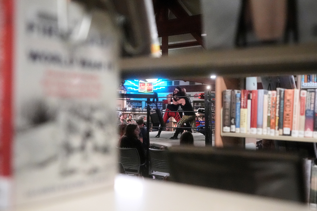 Wrestlers Loverboy Leo, middle left, and Joey Gonzo are seen through shelves of books during their match at a Lucha Libro pro wrestling event at Benicia Public Library Saturday, May 2, 2026, in Benicia, Calif. (AP Photo/Jeff Chiu)