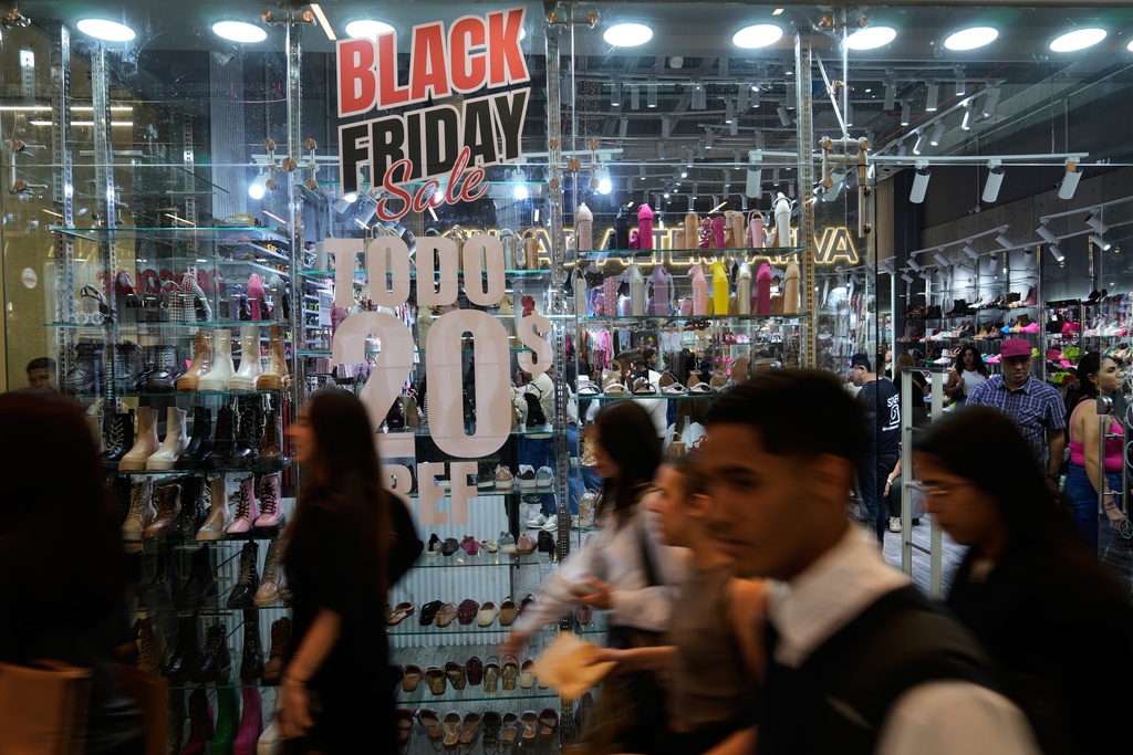 Mall shoppers walk past a banner promoting Black Friday discounts in Caracas, Venezuela, Friday, Nov. 28, 2025. (AP Photo/Ariana Cubillos)