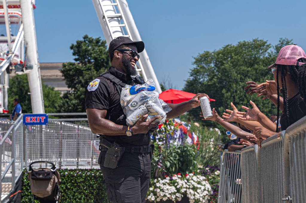 Children reach for cold bottles of water from U.S. National Park Police Officer R. Douglass as they wait in line for the ferris wheel at the Great American State Fair on the National Mall, Wednesday, July 1, 2026, in Washington. (AP Photo/Jen Golbeck)