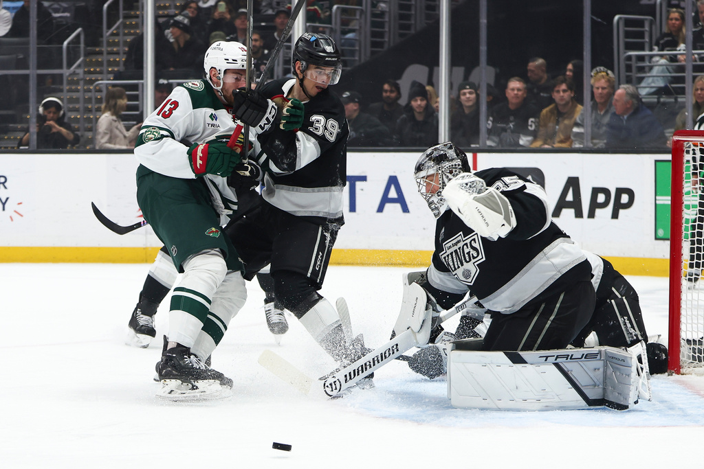 Los Angeles Kings goaltender Darcy Kuemper, right, makes a save as Minnesota Wild center Yakov Trenin (13) and Kings left wing Jeff Malott (39) watch during the first period of an NHL hockey game, Monday, Jan. 5, 2026, in Los Angeles. (AP Photo/Jessie Alcheh)
