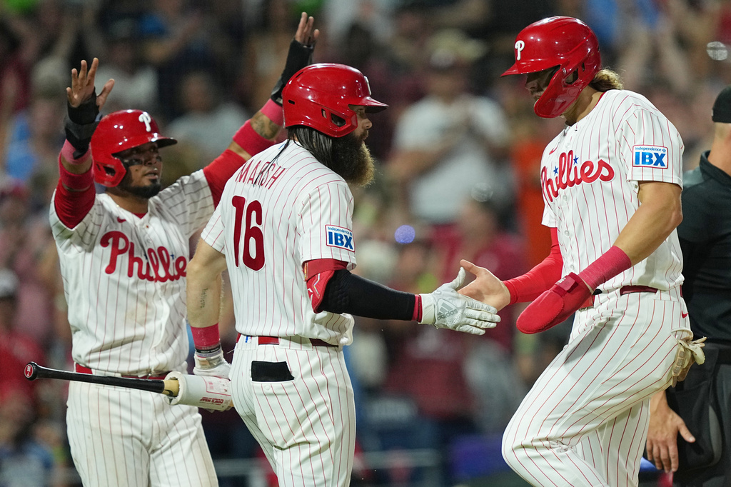 Philadelphia Phillies' Luis Arraez, left, and Alec Bohm, right, celebrate with Brandon Marsh (16) after scoring of an RBI double hit by Phillies Bryson Stott during the sixth inning of a baseball game against the Miami Marlins,Tuesday, Aug. 18, 2026, in Philadelphia. (AP Photo/Matt Rourke)
