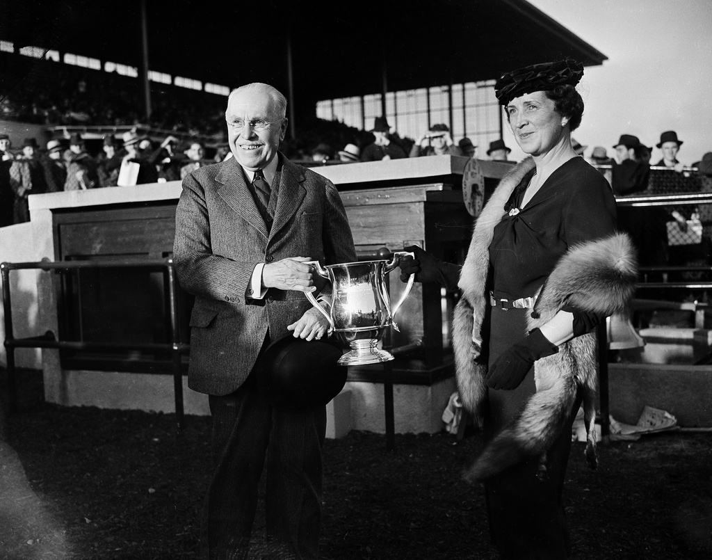 FILE- Samuel Riddle, left, owner of War Admiral, is presented with the trophy by Dorothy Butler wife of track owner James Butler Jr., after War Admiral won the Washington handicap horse race at Laurel Park, Md., Oct. 30, 1937. (AP Photo/Henry Griffin, File)