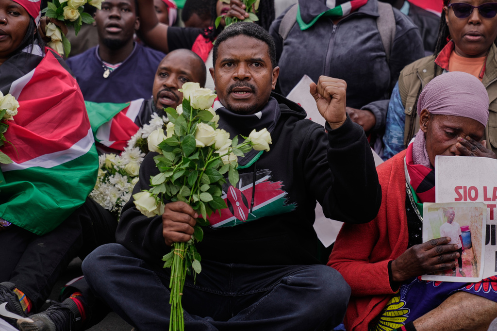 A protester gestures while holding flowers, during a demonstration marking two years since more than 60 people died in anti-government protests that resulted in the storming of the parliament, in Nairobi, Kenya, Thursday, June 25, 2026. (AP Photo/Brian Inganga)