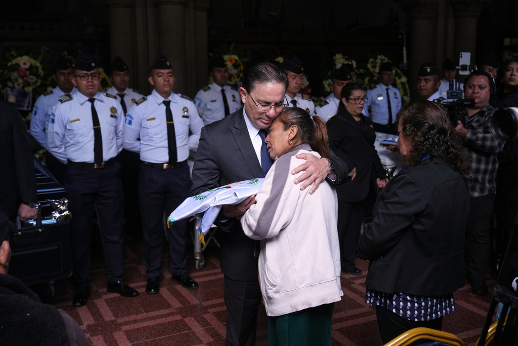 Interior Minister Marco Antonio Villeda gives a Guatemalan flag to the mother of police officer Luis Zetino, one of many officers killed while retaking control of three prisons, during a wake for the fallen officers at the Interior Ministry in Guatemala City, Monday, Jan. 19, 2026. (AP Photo/Moises Castillo)