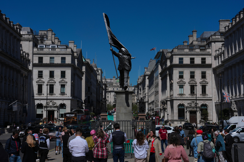 Members of the public look at a statue of a man holding a flag covering his face, and signed 'Banksy', which has appeared in Waterloo Place in London, Thursday, April 30, 2026. (AP Photo/Kin Cheung)