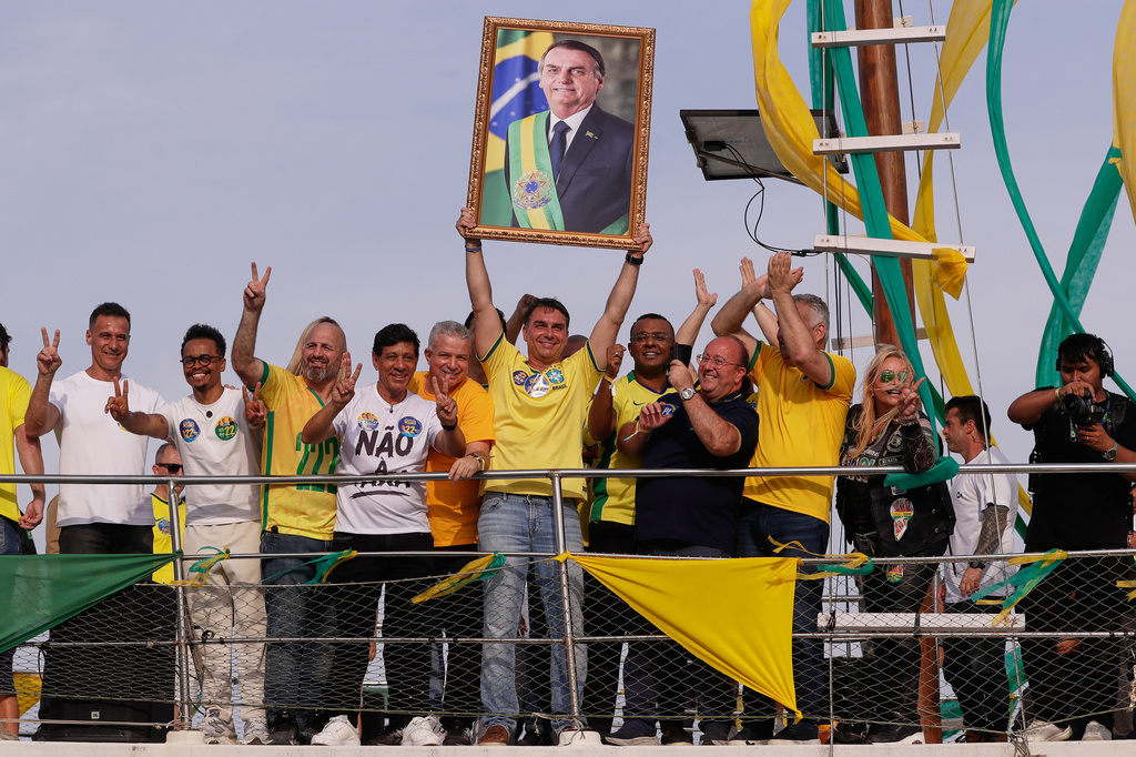 Opposition presidential candidate Flavio Bolsonaro holds a photo of his father, former President Jair Bolsonaro, as he rides a boat during a campaign rally ahead of the October general elections in Angra dos Reis, Rio de Janeiro state, Brazil, Saturday, Aug. 29, 2026. (AP Photo/Bruna Prado)