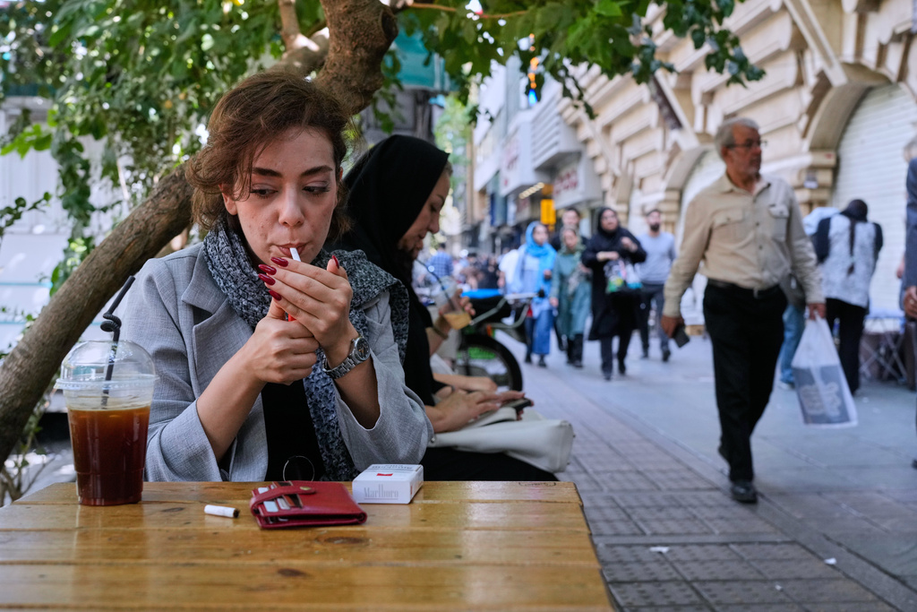 A woman lights a cigarette in the alfresco dining area of a cafe at the Enqelab-e-Eslami (Islamic Revolution) street, in Tehran, Iran, Saturday, Sept. 27, 2025. (AP Photo/Vahid Salemi)