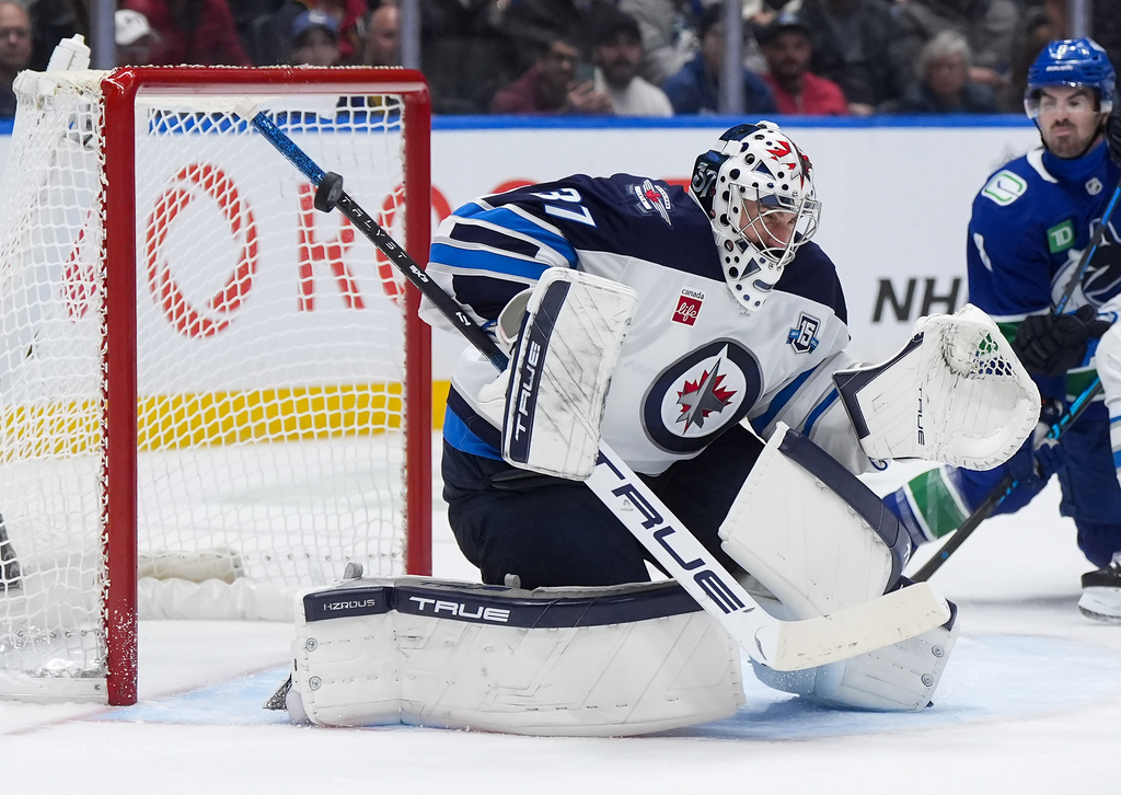 Winnipeg Jets goalie Connor Hellebuyck (37) makes a save with the shaft of his stick during the third period of an NHL hockey game against the Vancouver Canucks, in Vancouver, on Tuesday, Nov. 11, 2025. (Darryl Dyck/The Canadian Press via AP)