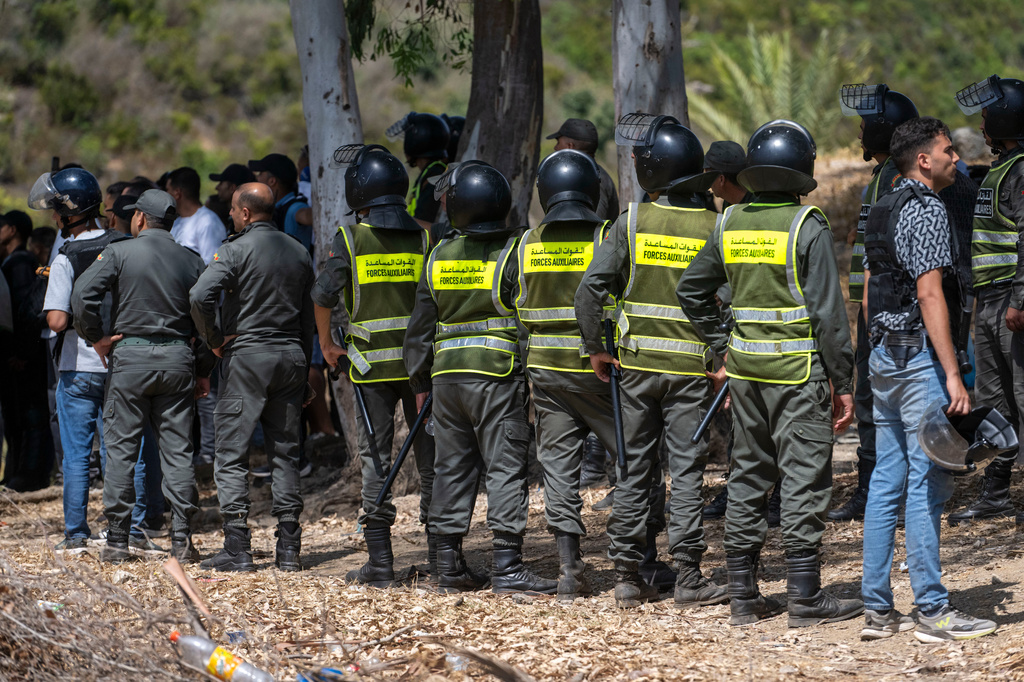 Moroccan security forces stand guard as migrants gather on a hill attempting to cross from the border town of Fnideq to the Spanish enclave of Ceuta, Saturday, Aug. 15, 2026. (AP Photo)
