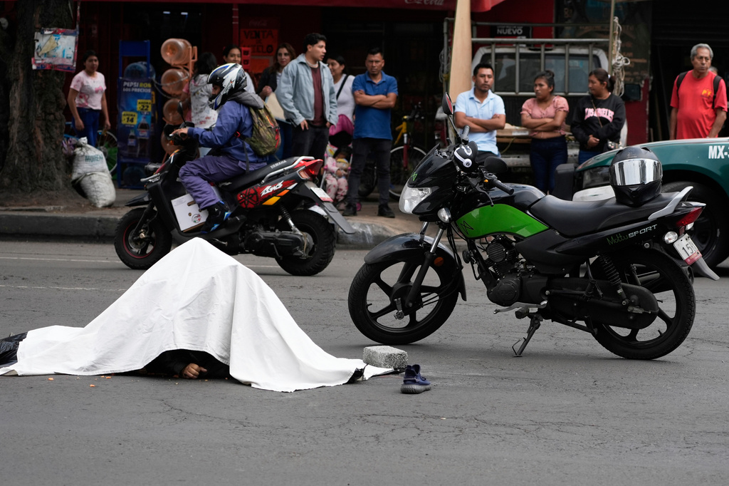 FILE - The body of a delivery person is covered by a white cloth as people watch police work the scene of a fatal traffic accident, in Mexico City, May 27, 2025. (AP Photo/Marco Ugarte, File)