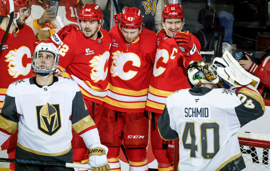 Vegas Golden Knights' Zach Whitecloud, front left, and goalie Akira Schmid, right, look away as Calgary Flames' Mikael Backlund, back right, celebrates after scoring during second-period NHL hockey game action in Calgary, Saturday, Dec. 20, 2025. (Jeff McIntosh/The Canadian Press via AP)