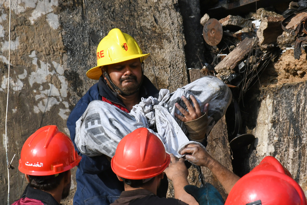 A firefighter carries remains of the victims after recovering from the rubble of a burnt building of a multi-story shopping plaza following a massive fire in Karachi, Pakistan, Monday, Jan. 19, 2026. (AP Photo/Ali Raza)