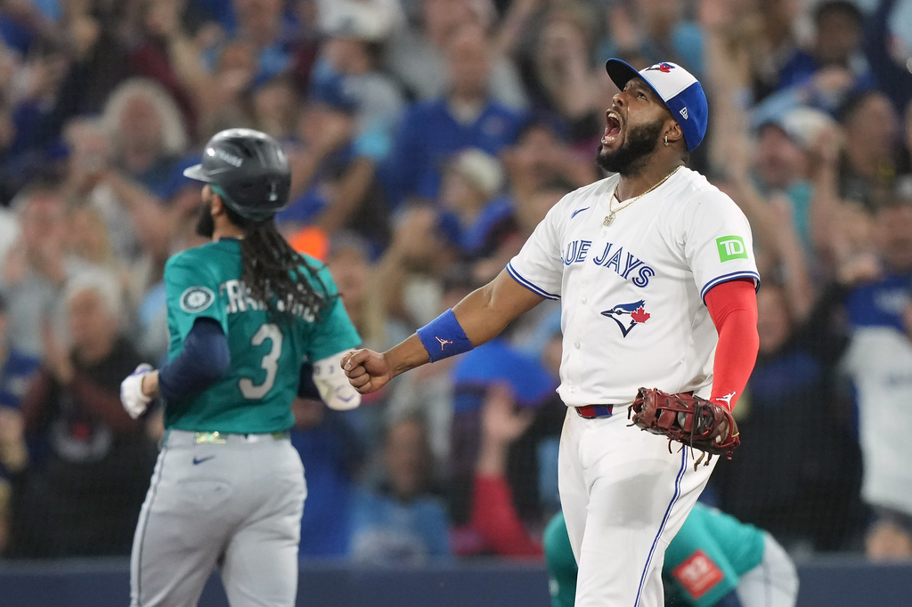 Toronto Blue Jays first base Vladimir Guerrero Jr. (27) celebrates an inning-ending double play as Seattle Mariners' J.P. Crawford (3) looks on during fourth inning MLB American League Championship Series game 6 baseball action in Toronto, Sunday, Oct. 19, 2025. (Nathan Denette/The Canadian Press via AP)