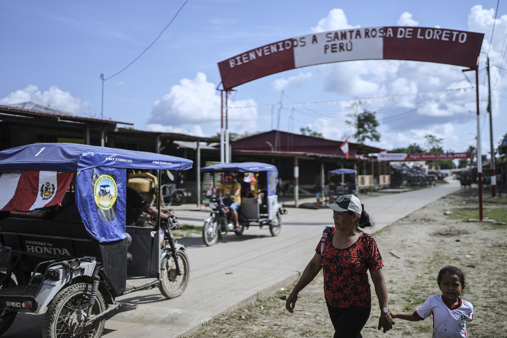 People walk along a street with a welcome sign to Santa Rosa, Peru, an island on the Amazon River at the center of a territorial dispute with Colombia, Monday, Aug. 18, 2025. (AP Photo/Ivan Valencia)