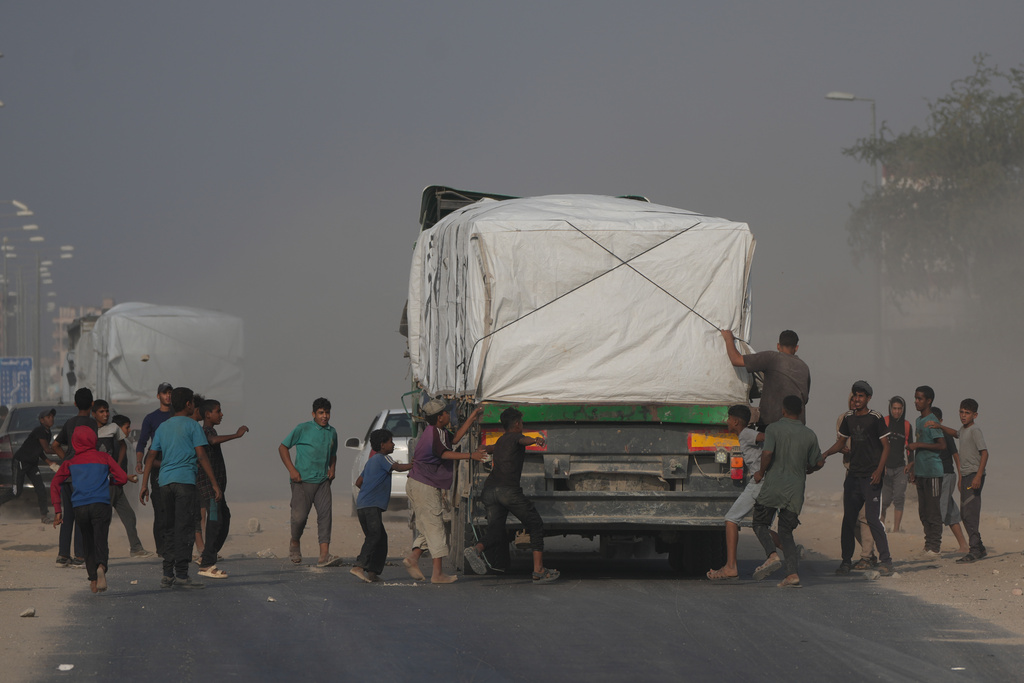 Palestinians rush toward trucks carrying aid as they drive through Deir al-Balah in central Gaza, Sunday, Nov. 9, 2025. (AP Photo/Jehad Alshrafi)