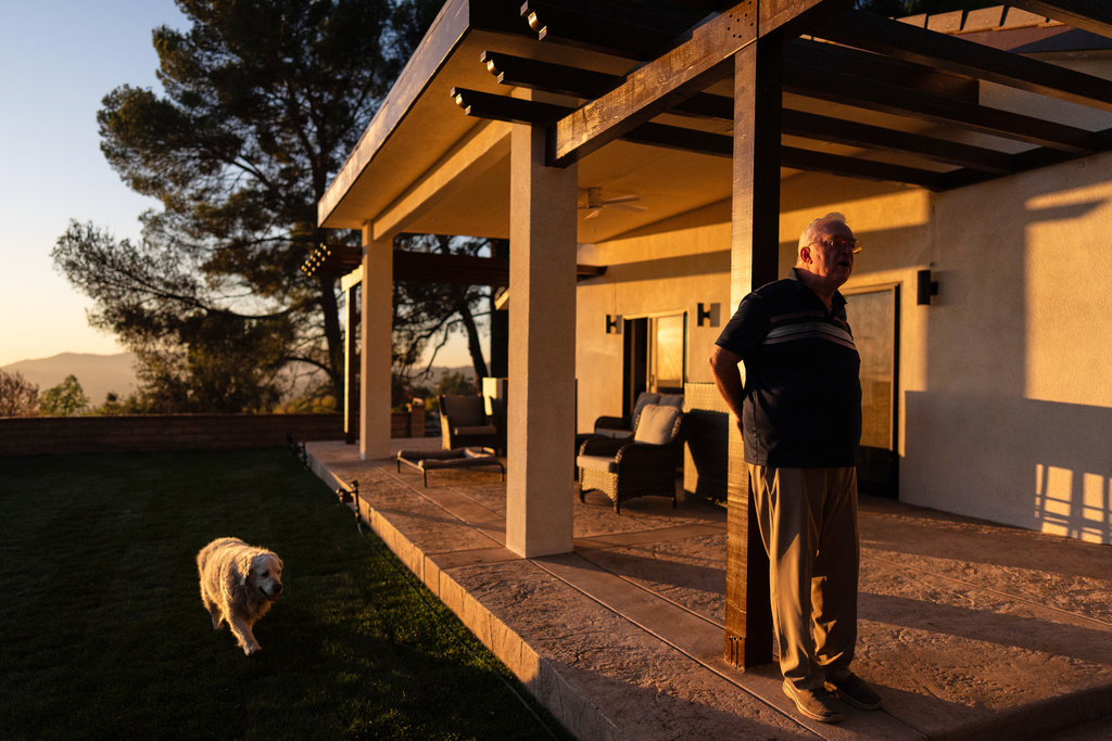 Ted Koerner, whose home was reduced to ash in the 2025 wildfires, stands on the porch of his newly rebuilt home, alongside his dog Daisy Mae, in Altadena, Calif., Dec. 11, 2025. (AP Photo/Jae C. Hong)