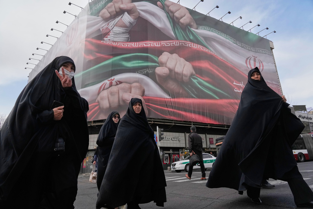 FILE - Women cross a street under a huge banner showing hands firmly holding Iranian flags as a sign of patriotism in Tehran, Iran, Jan. 14, 2026. (AP Photo/Vahid Salemi, File)