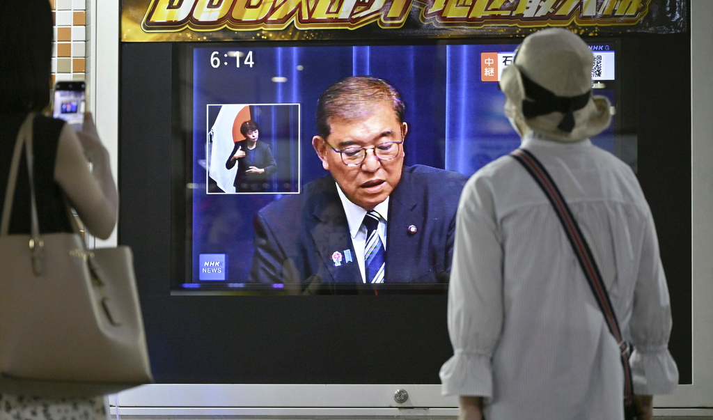 People look at a screen broadcasting a live TV news program showing Japanese Prime Minister Shigeru Ishiba speaking at a press conference, in Tokyo, Japan, Sunday, Sept. 7, 2025. (Kyodo News via AP)