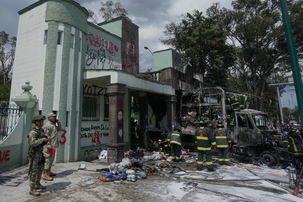 Soldiers and firefighters work the scene after demonstrators lit a garbage truck on fire during a protest marking the 11-year anniversary of the disappearance of 43 students from an Ayotzinapa rural teacher's college, outside the entrance of Campo Militar, in Mexico City, Thursday, Sept. 25, 2025. (AP Photo/Fernando Llano)