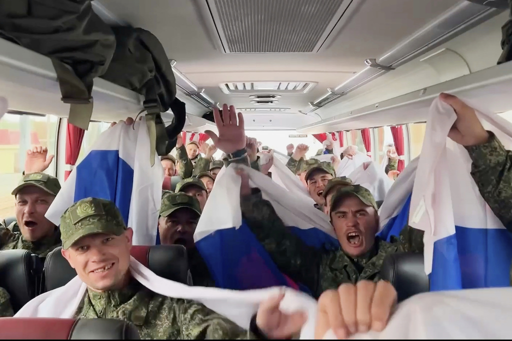 In this photo, taken from a video and distributed by the Russian Defense Ministry Press Service on Sunday, Aug. 24, 2025, Russian servicemen wave Russian national flags sitting in a bus at an exchange area in Belarus after returning from captivity during a POWs exchange of a group of servicemen between Russia and Ukraine. (Russian Defense Ministry Press Service via AP)