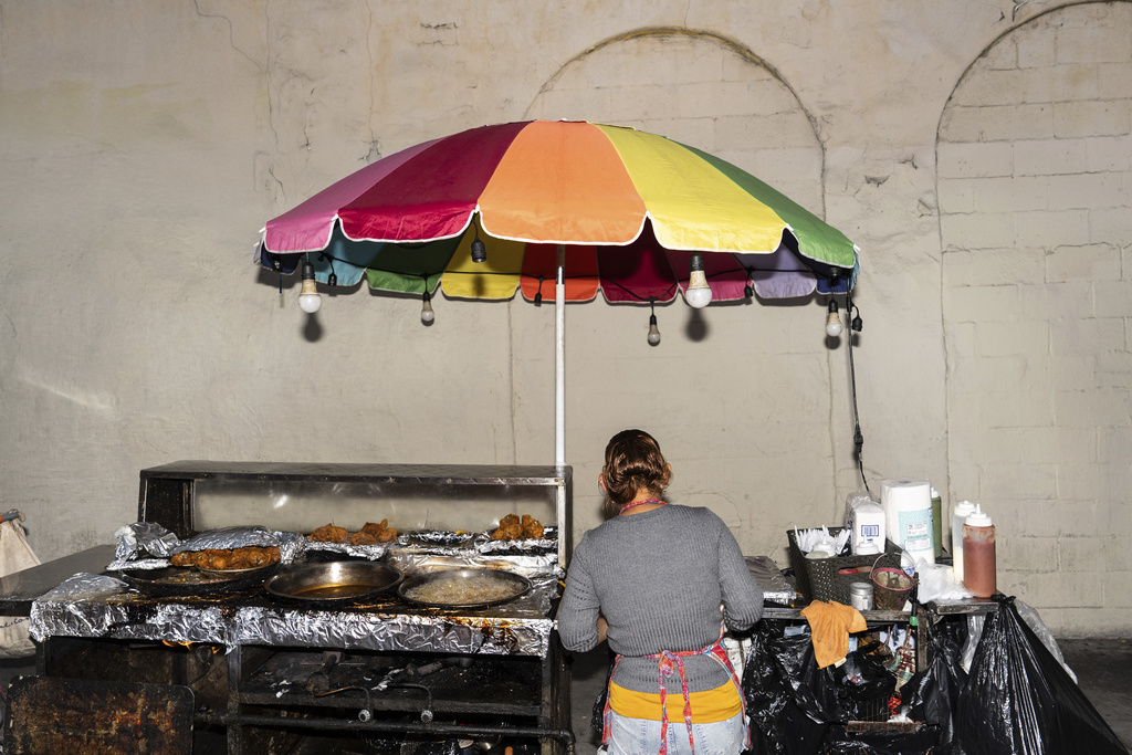 Street vendor Francisca, an immigrant from Guatemala, prepares an order at her cart in Los Angeles, Tuesday, Aug. 5, 2025, where her son accompanies her to help monitor their surroundings amid ongoing ICE raids. (AP Photo/Jae C. Hong)