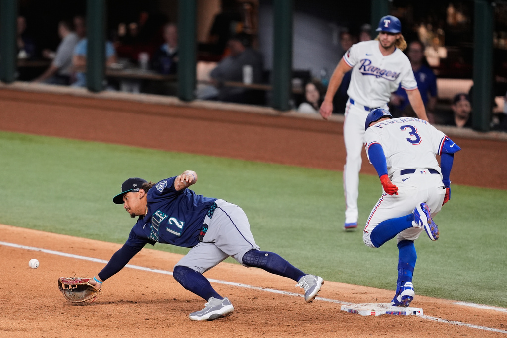 Texas Rangers' Joc Pederson (3) reaches on a single as Seattle Mariners first baseman Josh Naylor (12) dives for an errant throw to the bag in the fifth inning of a baseball game Tuesday, April 7, 2026, in Arlington, Texas. (AP Photo/Tony Gutierrez)