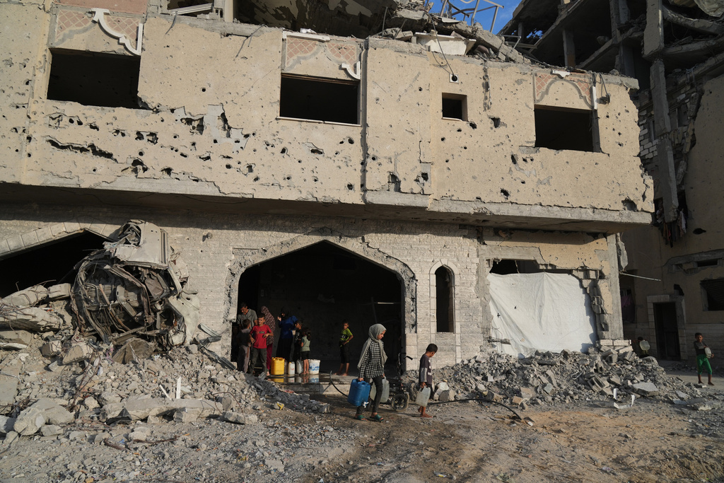 Displaced Palestinians collect water from a destroyed building in Khan Younis, Gaza Strip, Saturday, Oct. 18, 2025. (AP Photo/Jehad Alshrafi)