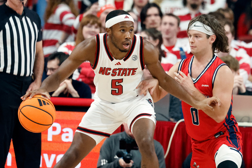 North Carolina State's Tre Holloman (5) looks to pass while battling Liberty's Colin Porter (0) during the first half of an NCAA college basketball game in Raleigh, N.C., Wednesday, Dec. 10, 2025. (AP Photo/Karl DeBlaker)