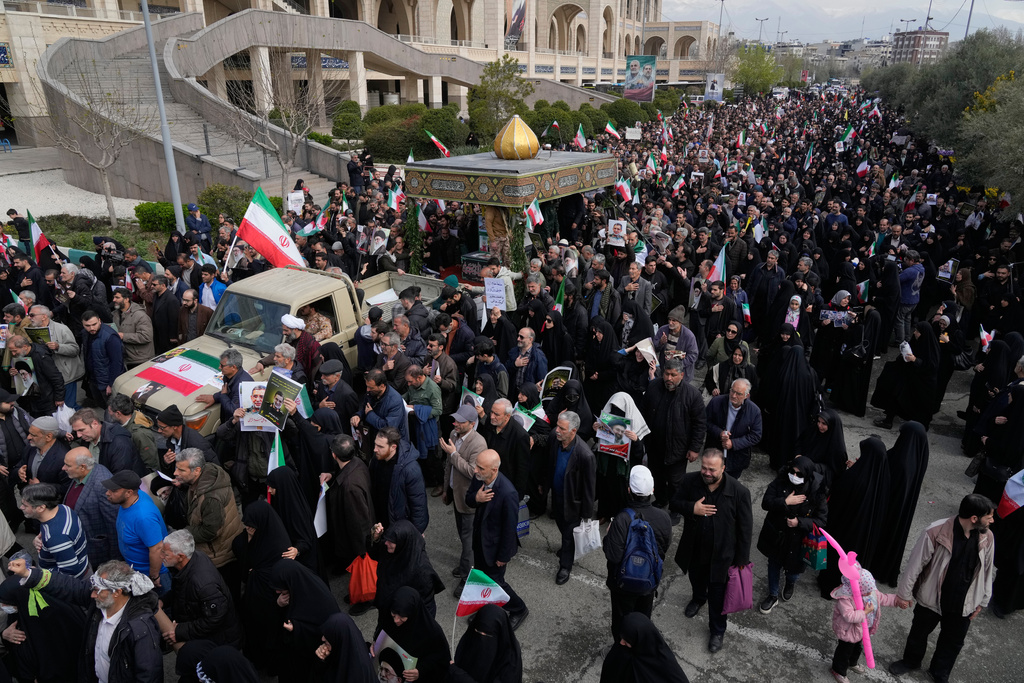 People follow a truck carrying the flag draped coffins of Gen. Ali Mohammad Naeini, a spokesperson for Iran’s paramilitary Revolutionary Guard and one of his comrades Amir Hossein Bidi , during their funeral procession in Tehran, Iran, Saturday, March 21, 2026. (AP Photo/Vahid Salemi)