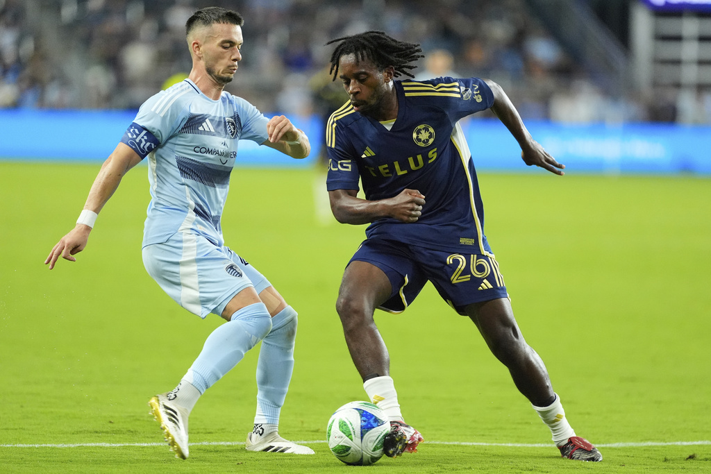 Vancouver Whitecaps midfielder Jean-Claude Ngando (26) kicks the ball past Sporting Kansas City midfielder Erik Thommy, left, during the second half of an MLS soccer match Saturday, Sept. 20, 2025, in Kansas City, Kan. (AP Photo/Charlie Riedel)