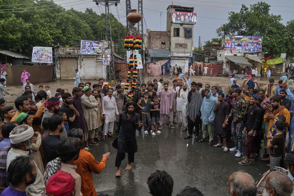 Devotees look at a performer balancing clay pot with an iron structure on his head as they attend celebrations of the three-day annual festival or 'Urs' of mystic and scholar, Hazrat Ali Hajveri, popularly known as Data Ganj Bakhsh at his shrine, in Lahore, Pakistan, Wednesday, Aug. 13, 2025. (AP Photo/K.M. Chaudary)