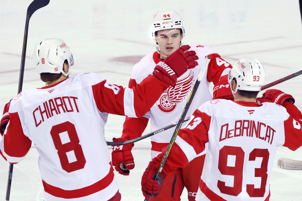 Detroit Red Wings' Axel Sandin-Pellikka (44) celebrates with Alex DeBrincat (93) and Ben Chariot (8) after scoring against the Calgary Flames during the first period of an NHL hockey game in Calgary, Alberta, on Wednesday, Dec. 10, 2025. (Larry MacDougal/The Canadian Press via AP)
