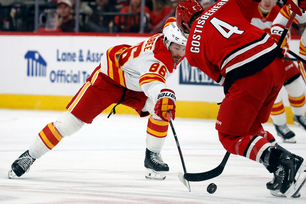 Calgary Flames' Joel Farabee (86) stretches for the puck as he approaches Carolina Hurricanes' Shayne Gostisbehere (4) during the first period of an NHL hockey game in Raleigh, N.C., Sunday, Nov. 30, 2025. (AP Photo/Karl DeBlaker)