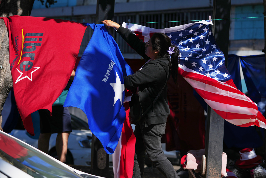 A street vendor hangs flags representing the National Party LIBRE, from left, the National Party, and the United States, near the national stadium in Tegucigalpa, Honduras, Saturday, Nov. 29, 2025, a day ahead of the general election. (AP Photo/Moises Castillo)