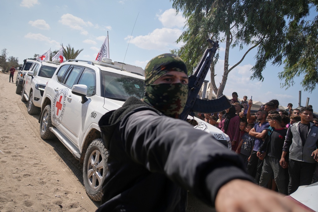 ICRC vehicles carrying released Israeli hostages make their way through groups of Palestinians and Hamas gunmen on their way to the Israeli border, in Khan Younis, southern Gaza Strip, Monday, Oct. 13, 2025. (AP Photo/Jehad Alshrafi)