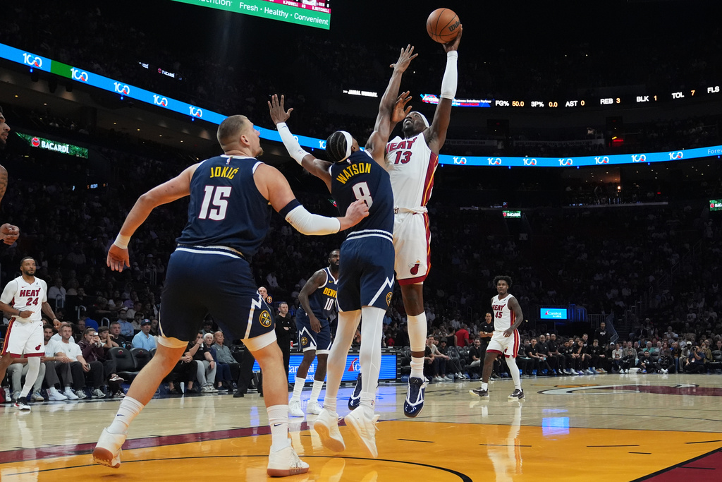 Miami Heat center Bam Adebayo (13) shoots as Denver Nuggets center Nikola Jokic (15) and guard Peyton Watson (8) defend during the first half of an NBA basketball game, Monday, Dec. 29, 2025, in Miami. (AP Photo/Lynne Sladky)