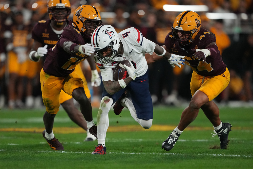 Arizona wide receiver Kris Hutson (4) runs between Arizona State defensive back Javan Robinson and linebacker Keyshaun Elliott (44) in the first half of an NCAA college football game, Friday, Nov. 28, 2025, in Tempe, Ariz. (AP Photo/Rick Scuteri)