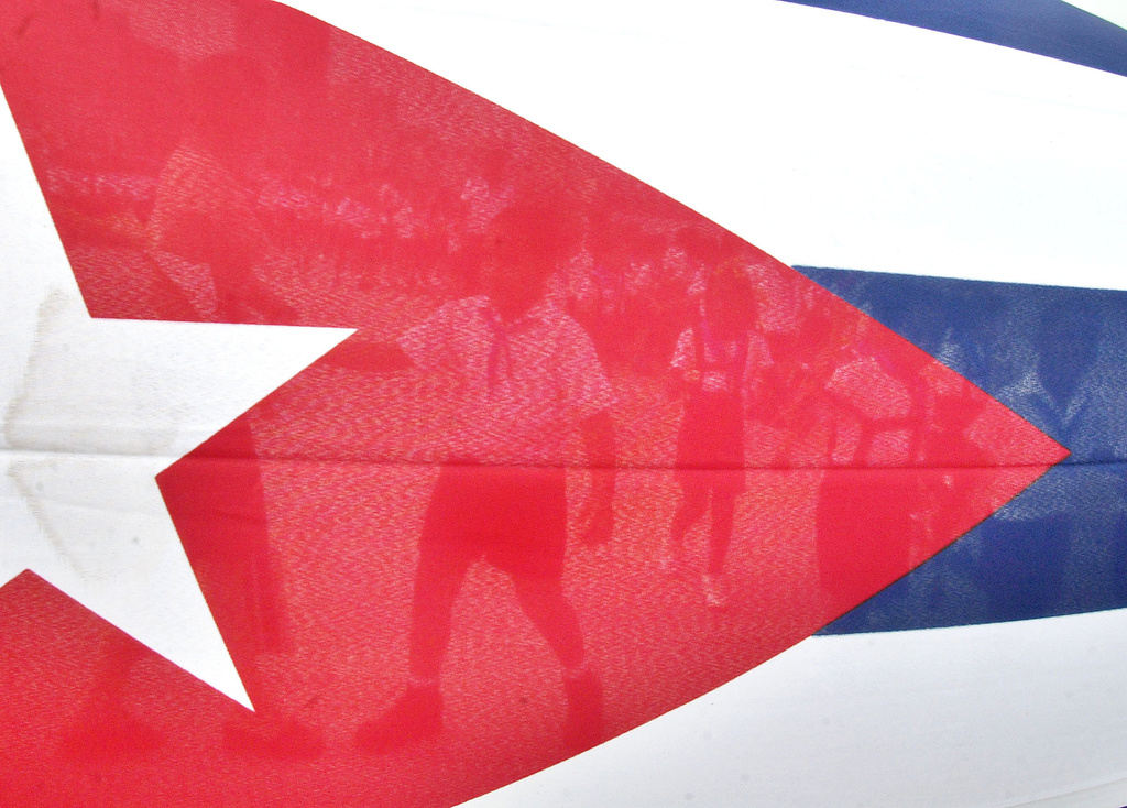 FILE - Children are seen through the Cuban flag while they walk to the Havana's Malecon to toss flowers into the ocean in commemoration of the anniversary of the death of the Cuban revolutionary Commander Camilo Cienfuegos, Thursday, Oct. 28, 2004 in Havana, Cuba. (AP Photo/Cristobal Herrera, File)